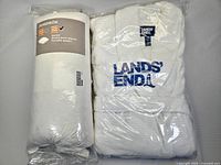 Photo showing the Lands' End 2X white bathrobe and queen-sized feather pillow both sealed in packaging, displaying the brand name and product details.