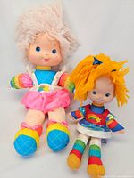 Large and smaller vintage Rainbow Brite dolls pictured sitting, showing colorful clothing and yarn hair details.