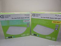 Two boxes of Commercial Electric 14-inch low profile square LED lights in bright white, one box open and one closed.