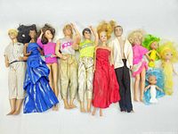 Full view of lot showing 11 vintage Barbie dolls laid out horizontally, various outfits and hair colors.