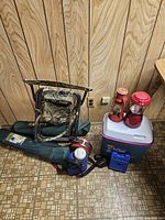 Photo of the lot including camo folding chair, two folded green chairs in bags, cooler, blue storage box, and two red lanterns.