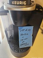 Close-up of black Keurig coffee machine with a handwritten note indicating lot and contents