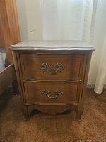 Front view of the wood nightstand showing two drawers and decorative metal handles in French Provincial style.