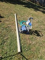 Electric power washer, green garden hose, and piece of gutter laid out on grass