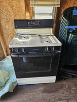 Front view of the gas stove showing four burners and black oven door with control panel above.