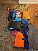 Photo shows three umbrellas, hats, face masks, a heated car seat pad, a pink patterned coin purse, and a wooden box arranged on carpet.