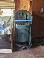 Stack of 14 green plastic outdoor chairs showing front and side profile with visible slats and armrests
