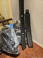 Black plastic gutter extension tubes leaning against a wall next to a bag of flexible corrugated hoses.