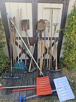 All yard tools leaning against an exterior wall, showing variety and quantity.