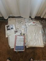 Several folded vintage tablecloths laid on carpet near window, some packaged in plastic, including a visible pink and blue checked tablecloth.