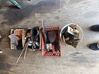 Overhead photo showing white bucket with tile floats and trowels, plastic crate with various tools and brown work gloves on floor.