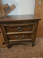 Front view of wooden nightstand showing two drawers with metal handles and decorative carvings.