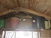Overview of the items placed on a wooden shelf inside a shed showing pots, watering can, and hanger stand.