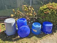 Four plastic tubs and trashcans placed outdoors against a garden fence.