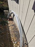 Six white curved garden arches leaning against a building, used for covering gardens with plastic or shade.