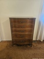 Full front view of the tall chest of drawers showing five curved front drawers and decorative metal handles in a cherry wood finish.