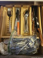Open drawer showing organized silverware such as forks, spoons, and knives in beige holders, plastic bag with additional spoons.
