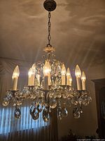Full view of vintage chandelier lit up showing metal arms, candle bulbs and hanging crystal teardrop prisms.