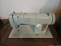 Front and side view of green Kenmore Model 65 sewing machine on wooden surface showing machine details.