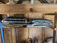 Four stacked vintage strap folding chairs with aluminum frames and blue/green striped fabric stored on a wooden shelf.