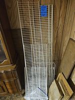 White wire shelving panels stacked against a wood-paneled wall with a blue note attached to largest panel.
