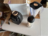 Vintage Oster blender black base, clear jar, and small blending cup with lid on table.