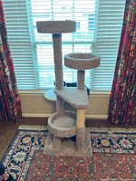 Front view of the cat tree showing multiple carpeted levels including two round platforms and the base cubby with visible wear on carpet and posts.