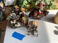 Photo showing the full nativity scene with multiple figurines and Santa on a bear figurine on a table surface, close to a plant.