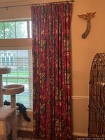 Curtains hanging from rod with floral pattern, pleated full length covering window and part of the wall.