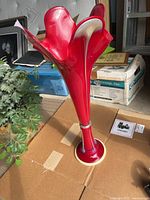 Tall red glass vase shown from an angle to reveal the sculptural, fluted design and base.