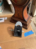 Photo showing the black hole punch placed on cardboard next to the base of the wooden clock.