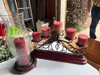 Wooden candelabra with five red candles and the hurricane candle holder with glass chimney and red candle on a white table.