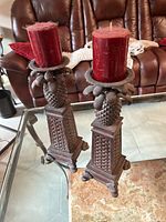 Two matching dark brown decorative candle holders with red pillar candles, featuring pineapple designs and detailed lattice bases.