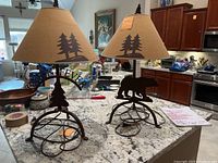 Photo of two matching iron lamps with tree motif bases and matching tree silhouette lampshades on kitchen island.