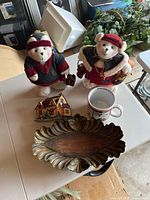 Photo showing two holiday-themed polar bear stuffed figurines, a decorative wooden tray, a holiday house figurine, and a holiday-themed ceramic mug.