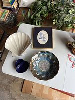 Photo of all four items on white table including white seashell bowl, decorative blue and brown ceramic bowl, small dark blue plate, and framed motivational writing with navy blue mat and gold frame