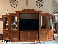 Front view of the wooden entertainment center with central TV space and two glass display cabinets on sides.