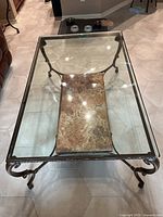 Photo showing full view of coffee table from above highlighting clear glass top and granite bottom shelf, metal frame with controlled curve legs.