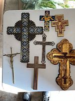 Top down view of all 7 hanging crosses on a white table, showing different styles and materials