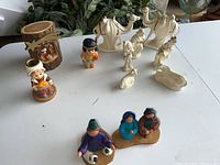 Wide photo showing all figurines: two Thanksgiving figurines, white porcelain nativity figures including camels, and clay nativity scene figures.