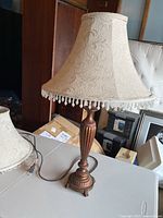 Photo of the lamp assembled with one lampshade on a table, showing the carved wooden base, fabric lampshade with embossed floral pattern and fringe trim.