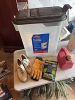 Full view of the lot items on a white table including men's shoes, gardening gloves, Duracell batteries, pet food dispenser, and pink gas tank container