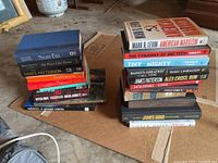 Photo showing two stacks of various non-fiction and fiction books on a concrete floor. Some visible titles include political books and thrillers.