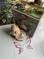 Solar fairy figurine light with clear orb and flower details beside its box, showing outdoor garden setting on the box.