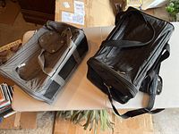 Two soft-sided cat carriers on table, one grey and one black, showing overall item condition and details.
