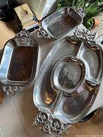 Three pewter items: one large oval serving tray and two matching rectangular bowls with decorative handles, displayed on table.