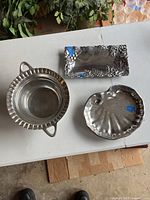 Overview of the set showing all three silver decorative items on a white table with plants in the background