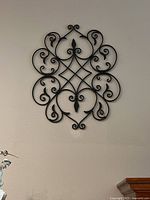 Front view of one wrought iron wall hanging with intricate scroll design hung on a white wall.