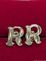 Front view of 10KT gold stud earrings shaped as the letter R on red background.