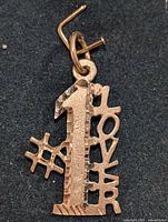 Close-up photo of the gold pendant showing the number '1', hashtag symbol, and 'LOVER' text detail.